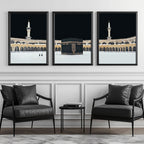 Set of 3 framed canvas triptych showing dramatic night views of Masjid Al-Haram with the Kaaba centered, glowing gold minarets and white marble courtyard against a deep black sky, displayed above a neutral sofa.