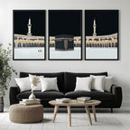 Set of 3 framed canvas triptych showing dramatic night views of Masjid Al-Haram with the Kaaba centered, glowing gold minarets and white marble courtyard against a deep black sky, displayed above a neutral sofa.