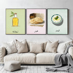 Set of 3 framed canvas triptych featuring illustrated olive oil bottle, flatbread and labneh bowl with Arabic calligraphy labels on soft green, pink and blue pastel backgrounds, displayed above a neutral sofa.