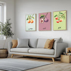 Set of 3 framed canvas triptych featuring soft watercolor botanical illustrations of pear, fig and apple branches with Arabic calligraphy labels on pastel mint, pink and green backgrounds, displayed above a neutral sofa.