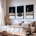 Set of 3 framed canvas triptych showing dramatic night views of Masjid Al-Haram with the Kaaba centered, glowing gold minarets and white marble courtyard against a deep black sky, displayed above a neutral sofa.