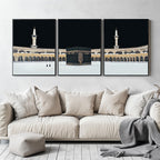 Set of 3 framed canvas triptych showing dramatic night views of Masjid Al-Haram with the Kaaba centered, glowing gold minarets and white marble courtyard against a deep black sky, displayed above a neutral sofa.