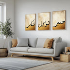 Set of 3 framed canvas triptych featuring Shukr, Tawakkul and Sabr in bold black Arabic calligraphy on a warm amber and cream textured background, displayed above a neutral sofa in a modern living room.