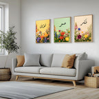 Set of 3 framed canvas triptych with Tawakkul, Sabr and Shukr in Arabic calligraphy above vibrant wildflower gardens on pastel yellow, green and peach backgrounds, displayed above a neutral sofa.