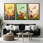 Set of 3 framed canvas triptych with Tawakkul, Sabr and Shukr in Arabic calligraphy above vibrant wildflower gardens on pastel yellow, green and peach backgrounds, displayed above a neutral sofa.