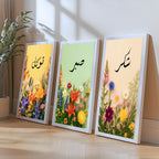 Set of 3 framed canvas triptych with Tawakkul, Sabr and Shukr in Arabic calligraphy above vibrant wildflower gardens on pastel yellow, green and peach backgrounds, displayed above a neutral sofa.