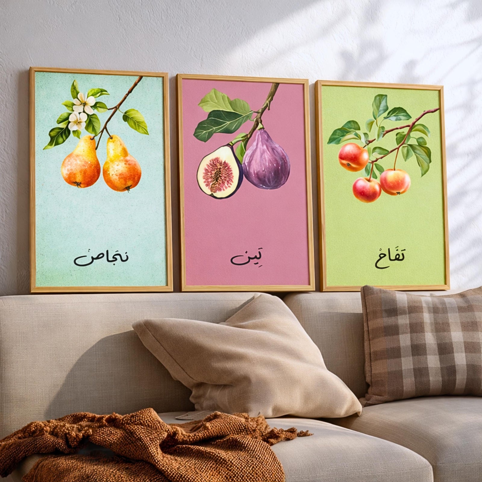 Set of 3 framed canvas triptych featuring soft watercolor botanical illustrations of pear, fig and apple branches with Arabic calligraphy labels on pastel mint, pink and green backgrounds, displayed above a neutral sofa.