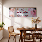 Panoramic artwork of two pink flamingos standing in shallow water facing each other with curved necks forming a heart shape. Gentle reflections ripple across the water while soft tropical foliage hangs above and pastel tones of pink and blush blend into the background of the wide horizontal bird composition.