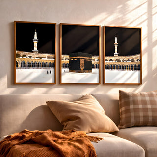 Set of 3 framed canvas triptych showing dramatic night views of Masjid Al-Haram with the Kaaba centered, glowing gold minarets and white marble courtyard against a deep black sky, displayed above a neutral sofa.