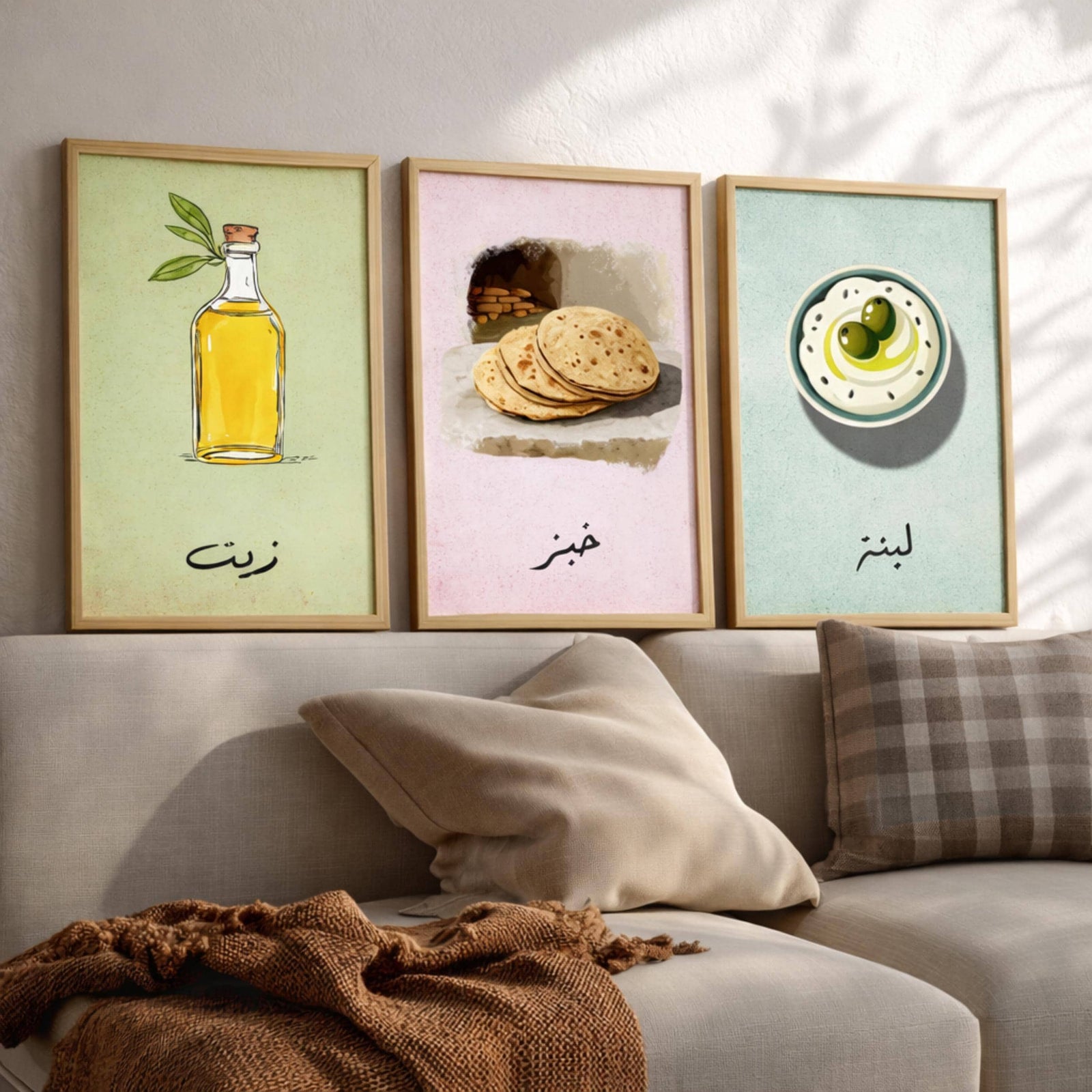 Set of 3 framed canvas triptych featuring illustrated olive oil bottle, flatbread and labneh bowl with Arabic calligraphy labels on soft green, pink and blue pastel backgrounds, displayed above a neutral sofa.