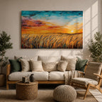 A framed canvas painting depicting a wheat field at sunset with golden stalks swaying under a vibrant sky blending orange, yellow, and blue hues. The artwork captures a rustic farmhouse landscape scene with textured brushstrokes emphasizing natural elements and an expansive horizon.