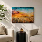A framed canvas painting depicting a wheat field at sunset with golden stalks swaying under a vibrant sky blending orange, yellow, and blue hues. The artwork captures a rustic farmhouse landscape scene with textured brushstrokes emphasizing natural elements and an expansive horizon.