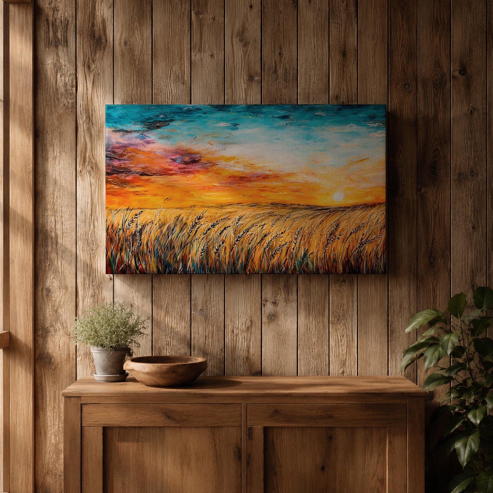 A framed canvas painting depicting a wheat field at sunset with golden stalks swaying under a vibrant sky blending orange, yellow, and blue hues. The artwork captures a rustic farmhouse landscape scene with textured brushstrokes emphasizing natural elements and an expansive horizon.