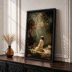 Framed artwork of Jesus praying in the Garden of Gethsemane, kneeling beneath a tree as soft rays of light shine down from above. Set in a modern living room, the canvas rests on a wooden console beside plants and neutral decor.