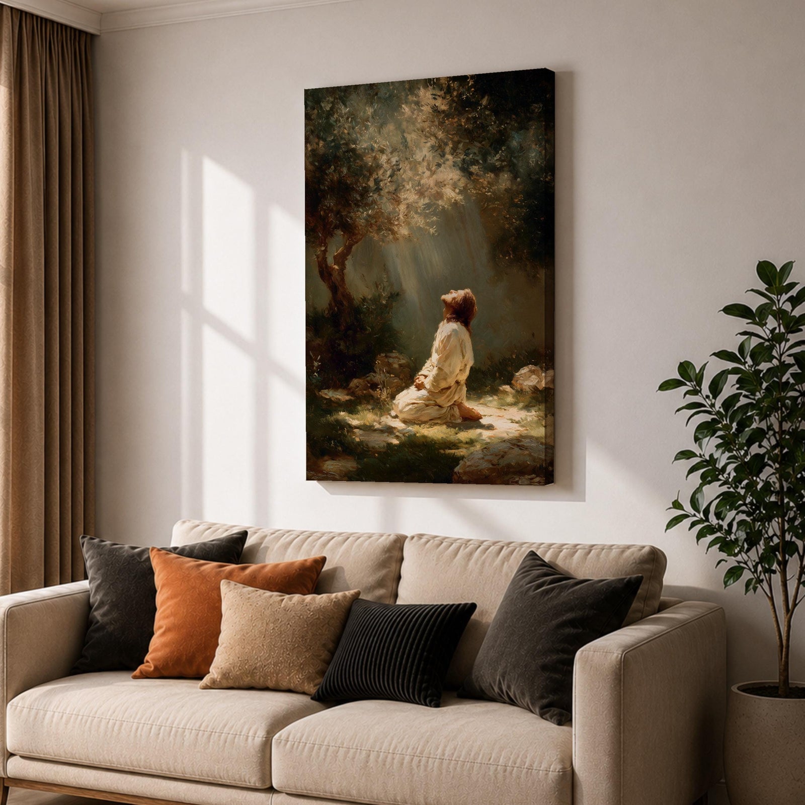 Framed artwork of Jesus praying in the Garden of Gethsemane, kneeling beneath a tree as soft rays of light shine down from above. Set in a modern living room, the canvas rests on a wooden console beside plants and neutral decor.