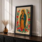 A framed stitched style art print depicting Our Lady of Guadalupe with hands clasped in prayer, surrounded by a radiant golden halo and vibrant floral embroidery in red, blue, and green. The image captures the traditional Mexican Catholic iconography with intricate textile detail and a serene expression.