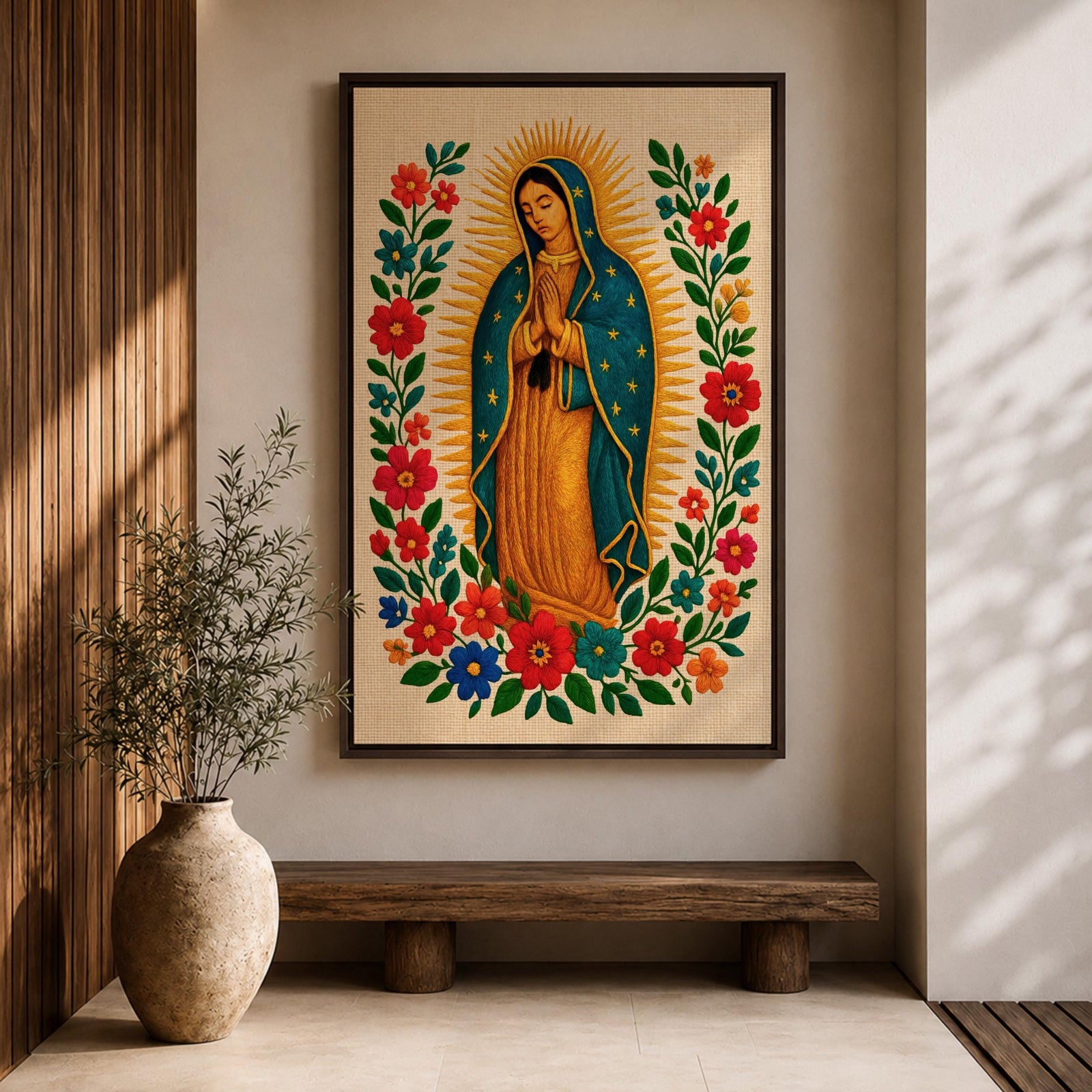 A framed stitched style art print depicting Our Lady of Guadalupe with hands clasped in prayer, surrounded by a radiant golden halo and vibrant floral embroidery in red, blue, and green. The image captures the traditional Mexican Catholic iconography with intricate textile detail and a serene expression.