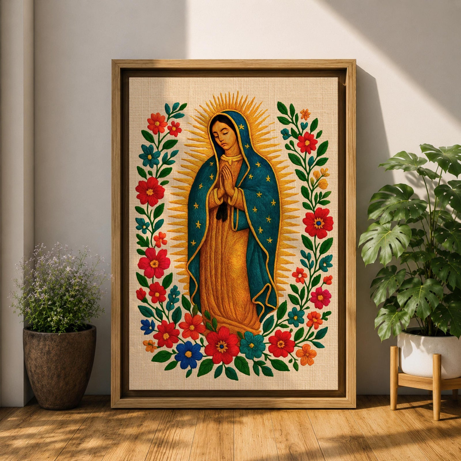 A framed stitched style art print depicting Our Lady of Guadalupe with hands clasped in prayer, surrounded by a radiant golden halo and vibrant floral embroidery in red, blue, and green. The image captures the traditional Mexican Catholic iconography with intricate textile detail and a serene expression.
