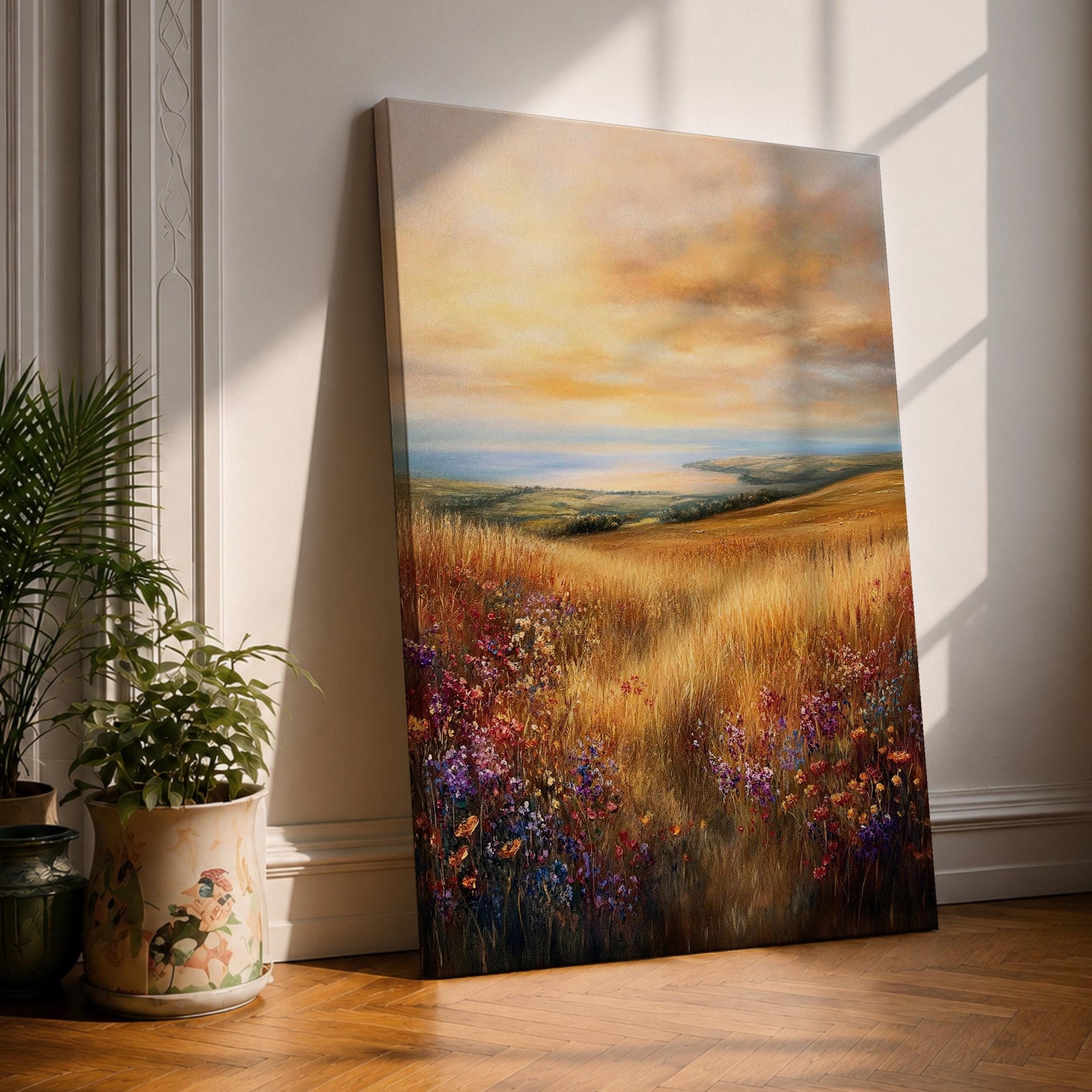 A framed canvas painting depicting a sunset meadow with tall golden grasses and wildflowers leading to a distant horizon under a dramatic sky. The artwork captures a serene rural landscape with warm tones and a cottagecore vibe, rendered in a classic oil painting style.