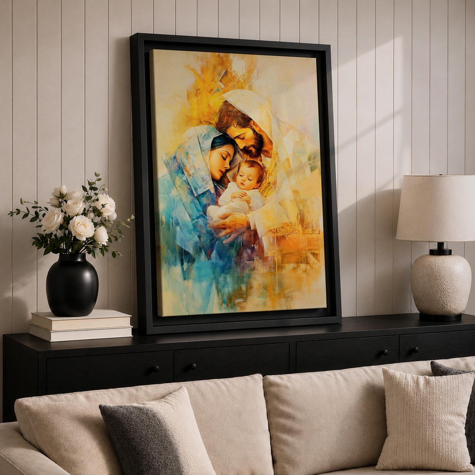 A framed canvas artwork depicting the Holy Family with Mary, Joseph, and baby Jesus in a tender embrace. The painting features warm tones and soft brush strokes, capturing the intimate moment of the Nativity scene with a focus on the figures' expressions and clothing details.