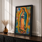 A vibrant framed canvas depicting Our Lady of Guadalupe, showing the Virgin Mary with hands clasped in prayer, wearing a blue mantle adorned with stars and a pink dress, surrounded by radiant golden rays and a colorful abstract background.