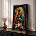 A vibrant framed canvas painting of Our Lady of Guadalupe depicts the Virgin of Guadalupe with hands clasped in prayer, wearing a teal mantle adorned with gold stars and surrounded by radiant light. The foreground features a colorful array of flowers, emphasizing the Catholic religious theme.