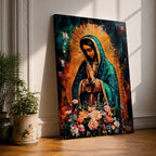 A vibrant framed canvas painting of Our Lady of Guadalupe depicts the Virgin of Guadalupe with hands clasped in prayer, wearing a teal mantle adorned with gold stars and surrounded by radiant light. The foreground features a colorful array of flowers, emphasizing the Catholic religious theme.