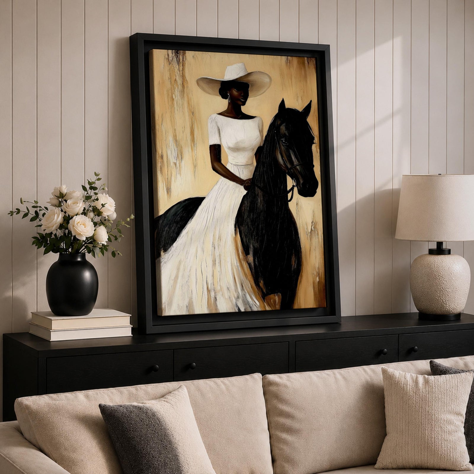 A framed painting of a woman dressed in a white dress and wide-brimmed hat riding a black horse. The artwork features a realistic style with warm beige and brown tones in the background, emphasizing the elegant posture of the rider and the horse’s strong presence.