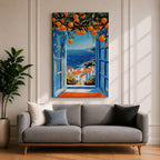 A vibrant framed canvas painting depicting an open Mediterranean-style window with blue shutters overlooking a coastal landscape. Above the window, ripe orange fruits hang from branches, framing a scenic view of white houses with terracotta roofs and a deep blue sea under a clear sky, rendered in a vivid, realistic style.