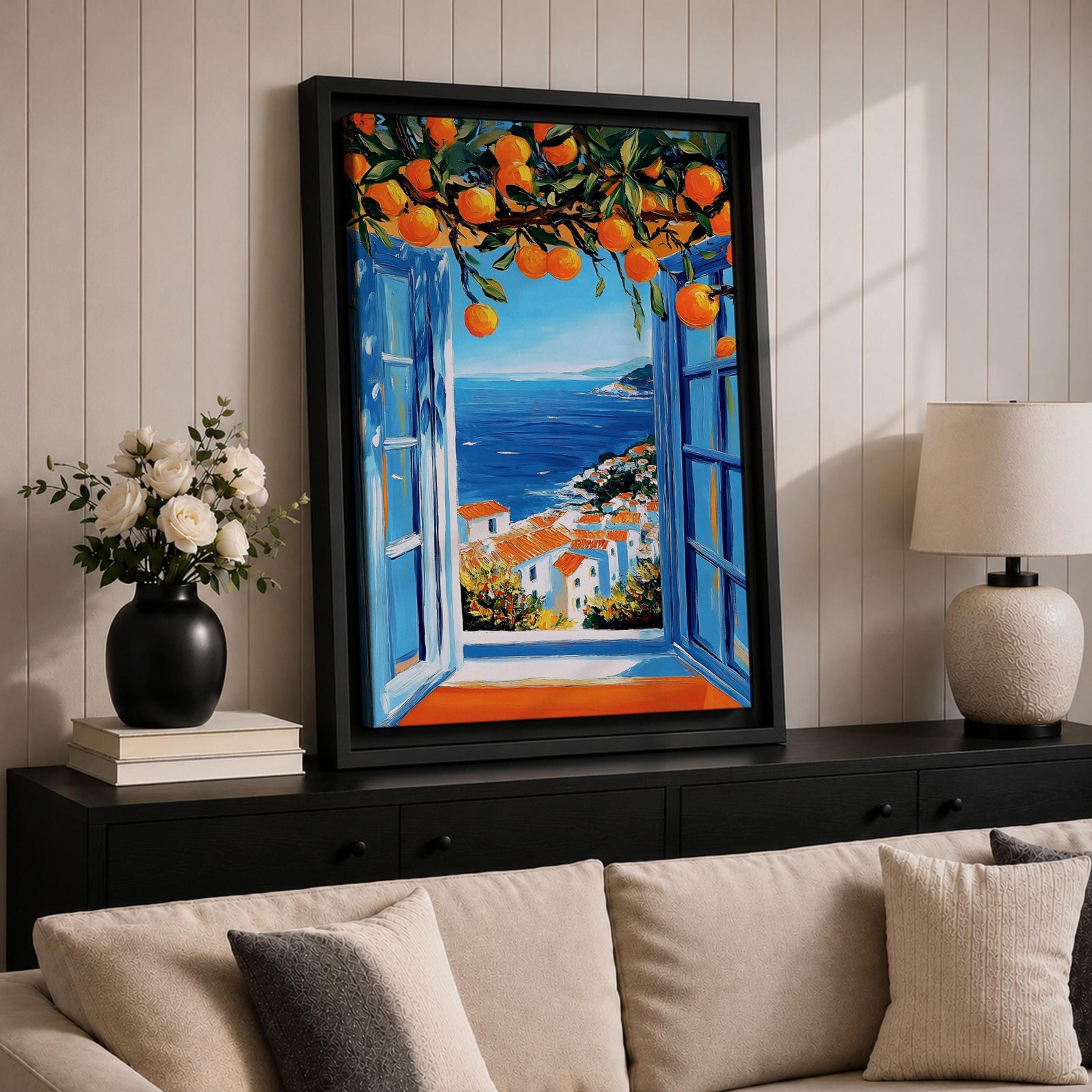 A vibrant framed canvas painting depicting an open Mediterranean-style window with blue shutters overlooking a coastal landscape. Above the window, ripe orange fruits hang from branches, framing a scenic view of white houses with terracotta roofs and a deep blue sea under a clear sky, rendered in a vivid, realistic style.