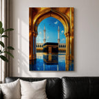 A vibrant framed canvas artwork depicting the Kaaba viewed through a golden arched doorway at Masjid Al Haram in Mecca. The scene shows the iconic black cube structure with gold detailing, two minarets in the background, and a reflective tiled floor under a bright blue sky with birds flying.