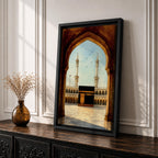 A watercolor style framed canvas depicting the Kaaba viewed through an arched gateway, showing the black cube structure with golden door and surrounding mosque minarets under a clear sky with flying birds, rendered in warm tones and detailed architectural elements.