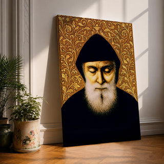 Portrait of Saint Charbel shown with a hooded monastic robe and long beard, eyes closed in prayerful contemplation, framed by ornate decorative patterns typical of devotional Christian iconography. The composition presents the Lebanese Maronite monk saint in a traditional religious portrait format emphasizing quiet devotion.