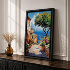 A vibrant framed canvas painting depicting a charming coastal village with stone-paved streets, terracotta rooftops, lush greenery, colorful flowers, and sailboats on a deep blue sea under a clear sky, rendered in a detailed, realistic style capturing Mediterranean summer ambiance.