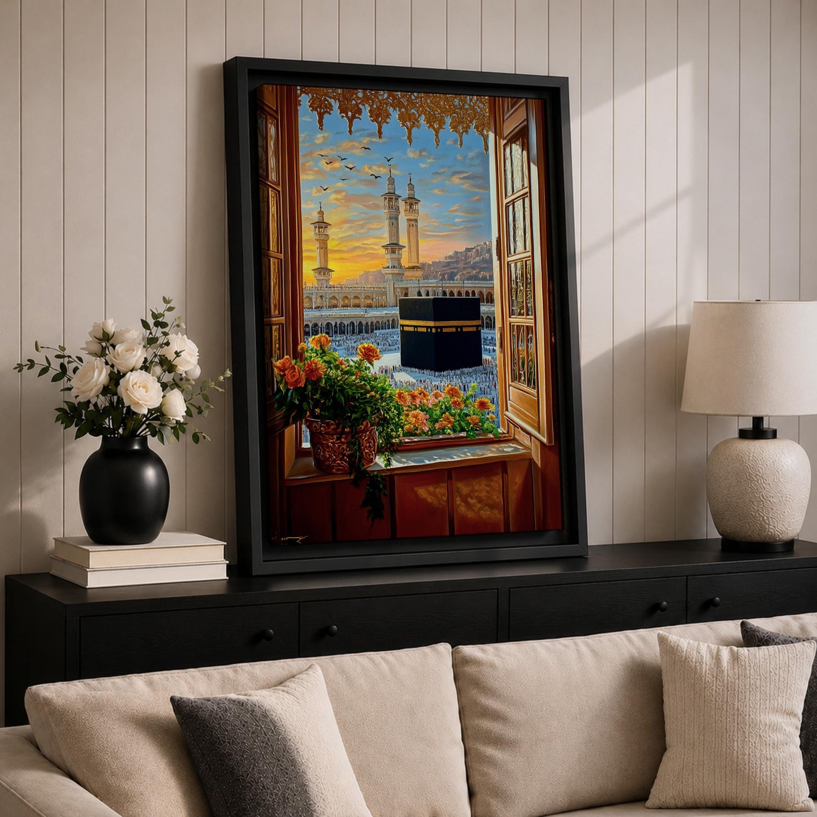 Painting of the Kaaba at Masjid Al Haram in Mecca viewed through an open wooden window with flowers on the sill, showing the black Kaaba in the courtyard surrounded by worshippers and tall mosque minarets under a glowing sunset sky.