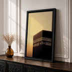 Minimalist artwork of the Kaaba at Masjid Al Haram in Mecca showing the black cubic shrine with gold calligraphy bands against a dramatic golden sunset sky and soft clouds.