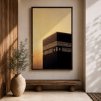 Minimalist artwork of the Kaaba at Masjid Al Haram in Mecca showing the black cubic shrine with gold calligraphy bands against a dramatic golden sunset sky and soft clouds.