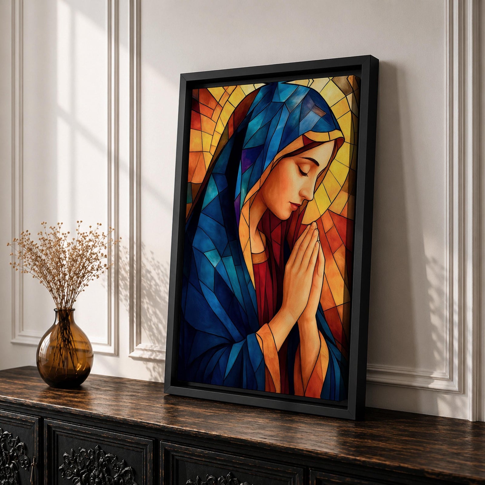 Stained glass style painting of the Virgin Mary shown in profile with head bowed and hands clasped in prayer, wearing a blue mantle and red garment, surrounded by geometric stained glass panels forming a radiant halo like background in a devotional Catholic Marian composition.