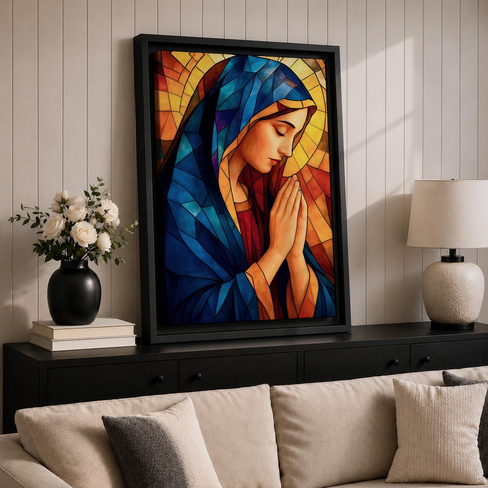 Stained glass style painting of the Virgin Mary shown in profile with head bowed and hands clasped in prayer, wearing a blue mantle and red garment, surrounded by geometric stained glass panels forming a radiant halo like background in a devotional Catholic Marian composition.