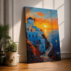 An impasto style framed canvas painting depicting a Santorini sunset over whitewashed buildings with a windmill on a cliffside overlooking the sea. The vibrant sunset sky reflects on the water with a small sailboat visible, capturing a Mediterranean coastal landscape scene with textured brushstrokes.