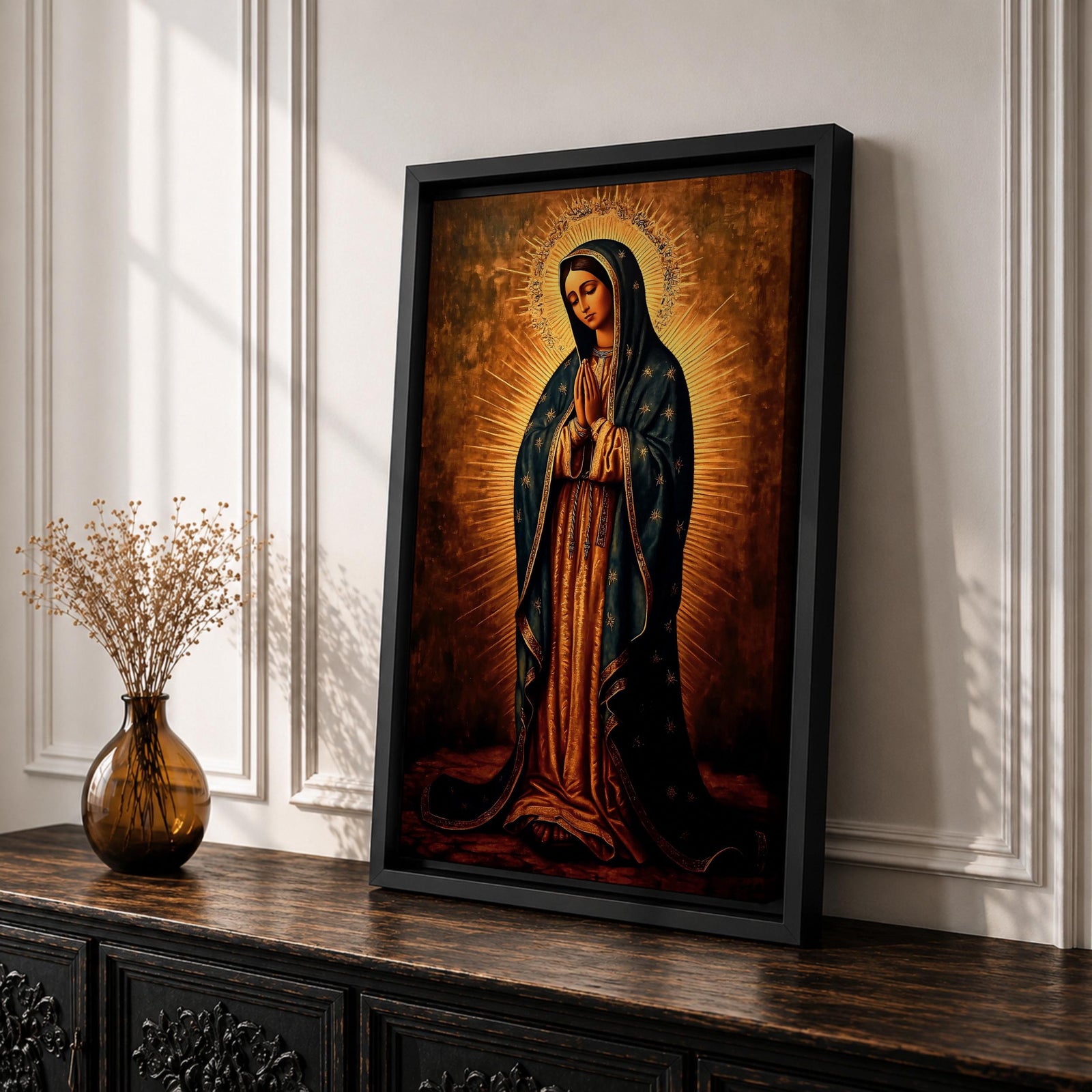 Painting of Our Lady of Guadalupe standing with hands clasped in prayer, wearing a long rose gown and dark star covered mantle, surrounded by radiant golden rays forming a halo behind her figure. The composition presents the Virgin in a traditional devotional icon style with serene expression and symmetrical vertical framing.