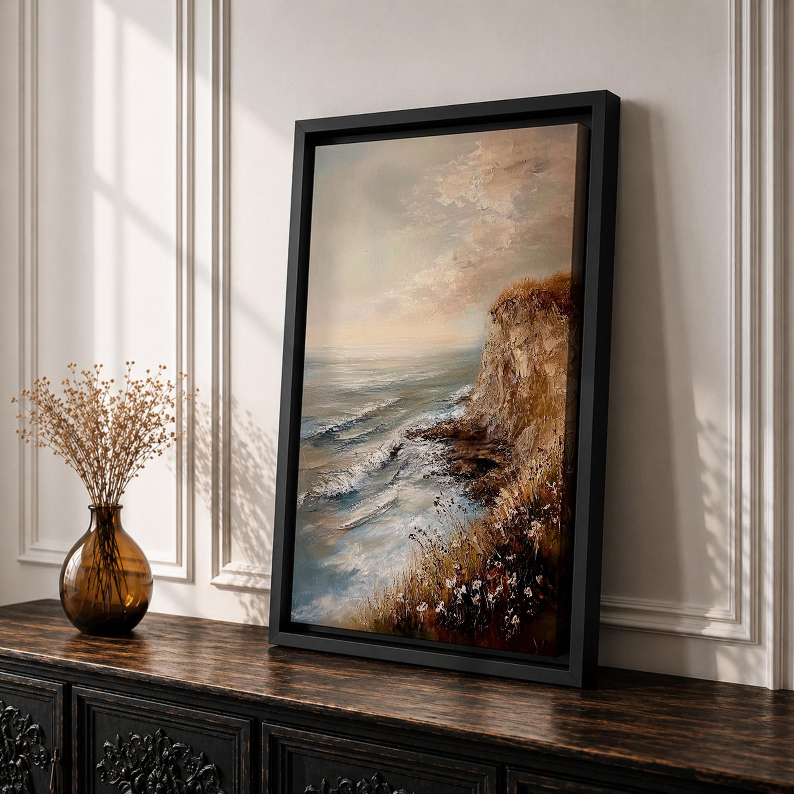 A vintage style framed canvas painting depicting a cliffside ocean seascape with waves crashing against rocky shores and wildflowers in the foreground. The textured brushwork captures the coastal landscape atmosphere with muted tones and a soft sky blending into the horizon.