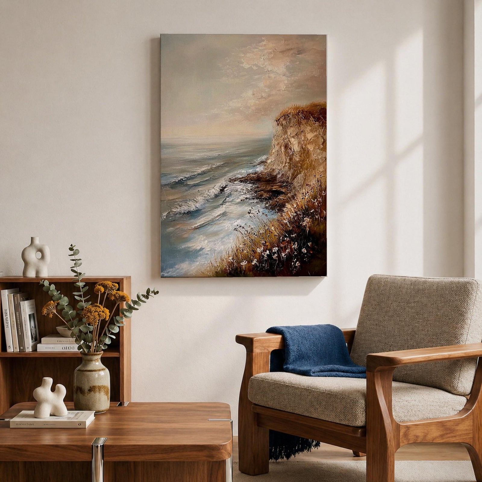 A vintage style framed canvas painting depicting a cliffside ocean seascape with waves crashing against rocky shores and wildflowers in the foreground. The textured brushwork captures the coastal landscape atmosphere with muted tones and a soft sky blending into the horizon.