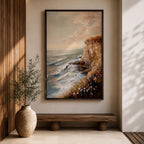 A vintage style framed canvas painting depicting a cliffside ocean seascape with waves crashing against rocky shores and wildflowers in the foreground. The textured brushwork captures the coastal landscape atmosphere with muted tones and a soft sky blending into the horizon.