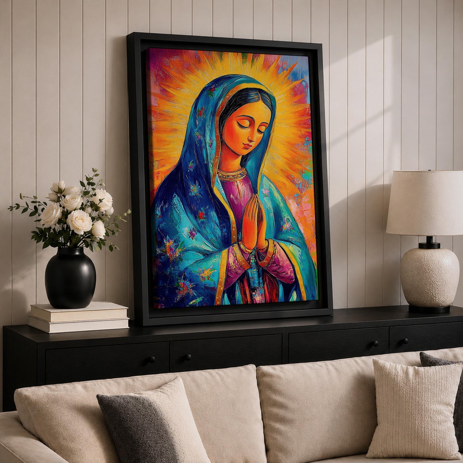 Colorful devotional painting of Our Lady of Guadalupe shown with hands clasped in prayer, wearing a blue star covered mantle over a rose dress while radiant golden rays form a glowing halo behind her figure. The composition presents the Virgin Mary in a vibrant painterly style with bold brushstrokes and centered sacred portrait.