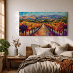A panoramic vineyard landscape painting showing long rows of grapevines covered in red and golden autumn leaves stretching toward distant mountains beneath a bright sky. Purple grape clusters hang beside the vines while a central path leads through the field, capturing a colorful wine country valley with bold impressionist brushstrokes.