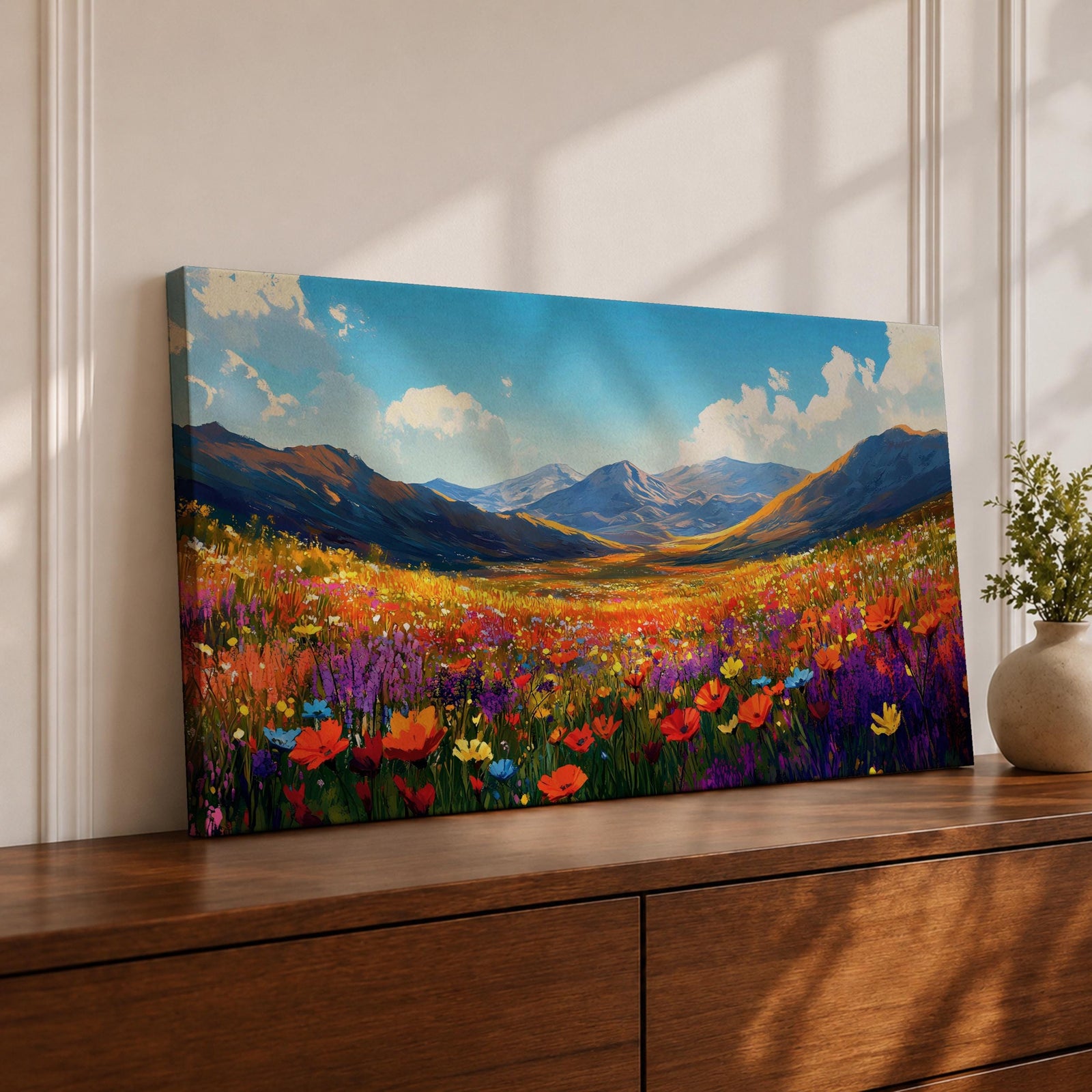 Panoramic painting of a vibrant mountain meadow filled with colorful wildflowers stretching toward distant alpine peaks. Red, yellow, purple, and blue blossoms cover the valley floor beneath a bright sky with soft clouds, while layered mountains rise along the horizon in a luminous natural landscape.