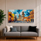 Panoramic painting of Oaxaca cathedral rising above a colorful colonial street lined with bright orange and yellow buildings. The historic Mexican architecture features twin cathedral towers beneath a dramatic blue sky with expressive painterly brushstrokes.
