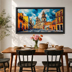 Panoramic painting of Oaxaca cathedral rising above a colorful colonial street lined with bright orange and yellow buildings. The historic Mexican architecture features twin cathedral towers beneath a dramatic blue sky with expressive painterly brushstrokes.