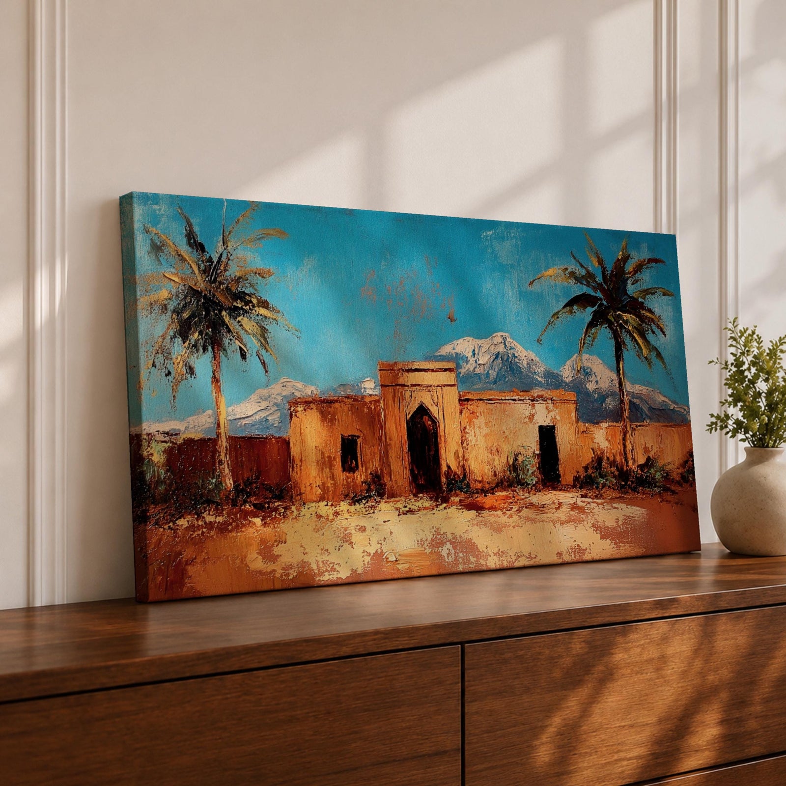 Panoramic painting of a Moroccan kasbah surrounded by palm trees in a desert oasis with the Atlas Mountains rising in the distance. The warm earthen architecture contrasts with a bright blue sky and textured brushstrokes capturing North African landscape scenery.